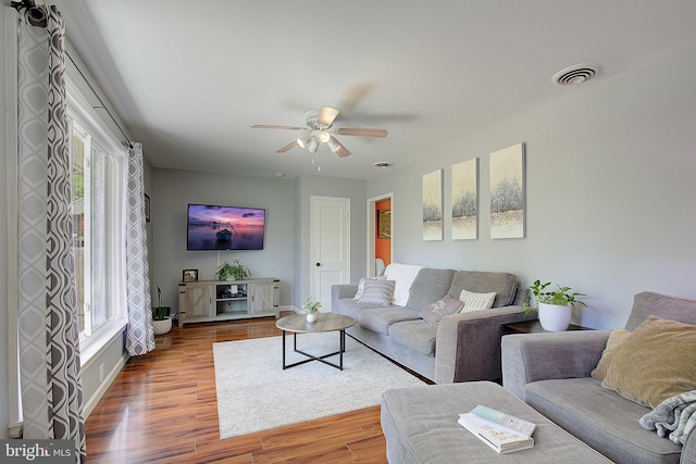 living area with baseboards, visible vents, wood finished floors, and ceiling fan