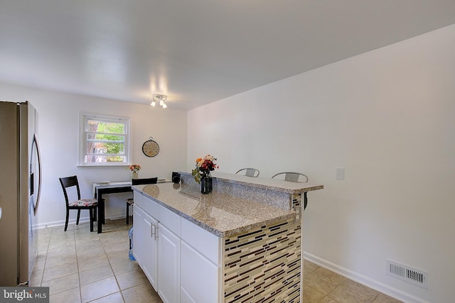 kitchen with light stone countertops, light tile patterned floors, stainless steel fridge, visible vents, and white cabinets