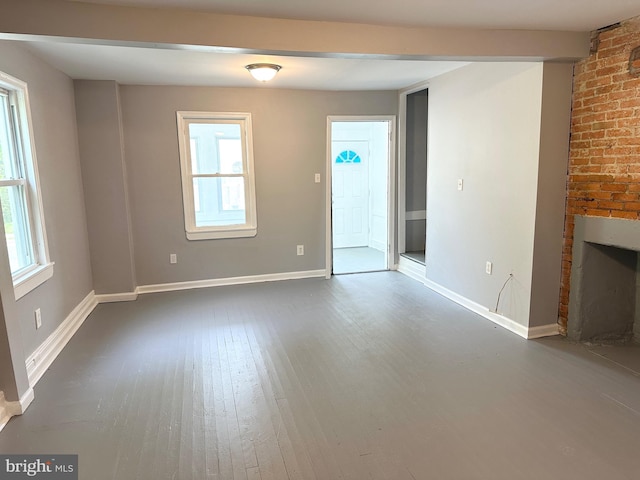 unfurnished living room with a brick fireplace, dark wood-style floors, brick wall, and baseboards
