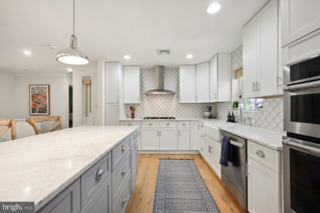 kitchen featuring gray cabinetry, white cabinets, stainless steel appliances, and wall chimney exhaust hood