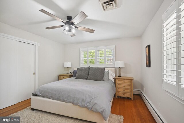 bedroom featuring ceiling fan, a baseboard radiator, wood finished floors, and visible vents