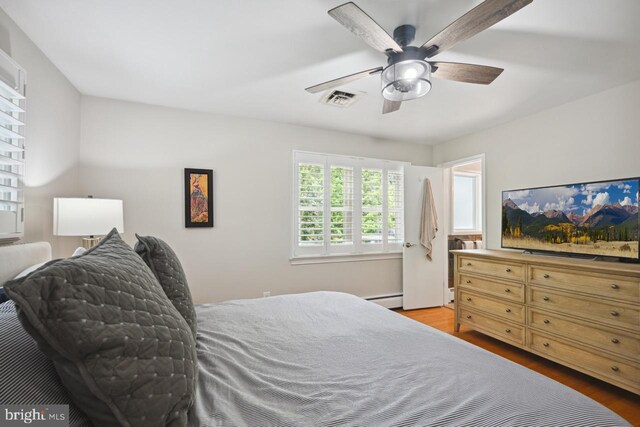 bedroom featuring visible vents, ceiling fan, wood finished floors, and baseboard heating