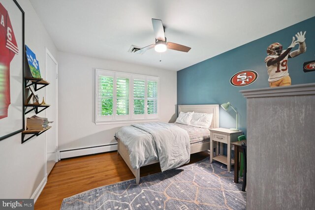 bedroom featuring a ceiling fan, visible vents, wood finished floors, and a baseboard radiator
