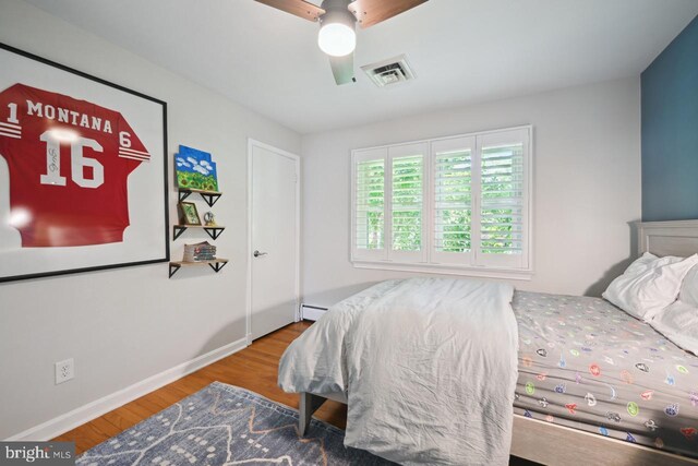 bedroom featuring visible vents, wood finished floors, baseboards, a baseboard heating unit, and a ceiling fan