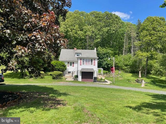 view of front of house featuring a garage, a front lawn, a forest view, and a chimney