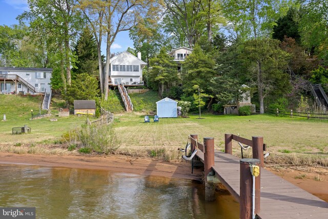 dock area featuring fence, a water view, and a lawn