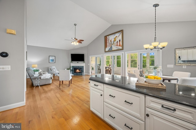 kitchen with decorative light fixtures, ceiling fan with notable chandelier, white cabinetry, high vaulted ceiling, and a lit fireplace