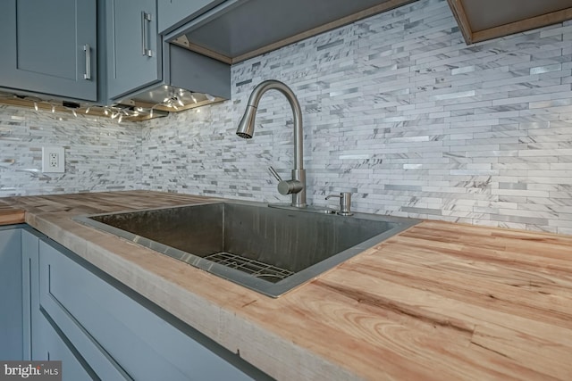 kitchen view of wooden counters, a sink, backsplash, and blue cabinets
