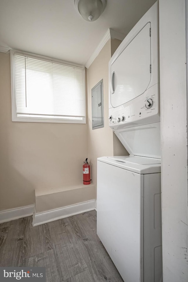 clothes washing area with stacked washer and clothes dryer, electric panel, crown molding, dark wood-style floors, and baseboards
