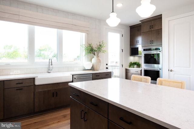 kitchen with a sink, appliances with stainless steel finishes, dark brown cabinets, light wood finished floors, and decorative light fixtures