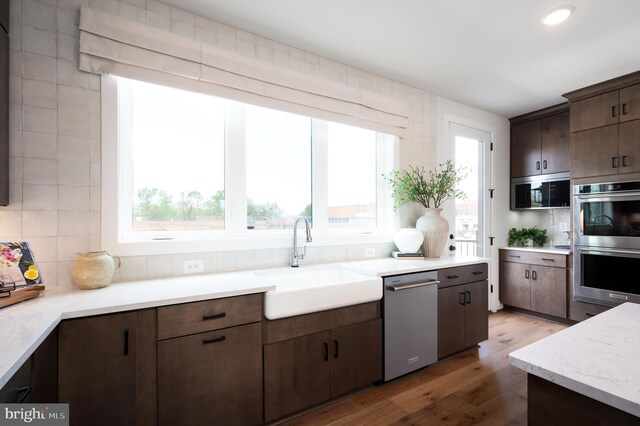 kitchen with appliances with stainless steel finishes, a healthy amount of sunlight, light wood finished floors, and a sink