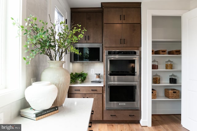 kitchen with dark brown cabinets, light countertops, light wood finished floors, and double oven