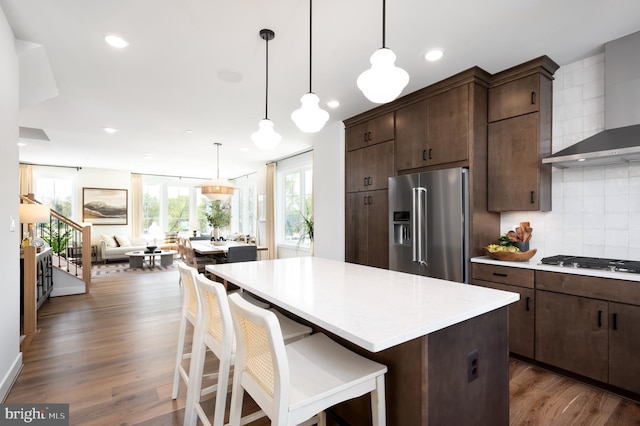 kitchen with high quality fridge, light countertops, gas cooktop, recessed lighting, and wall chimney exhaust hood