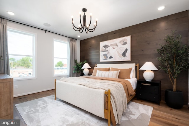 bedroom featuring wood finished floors, a chandelier, baseboards, an accent wall, and wooden walls
