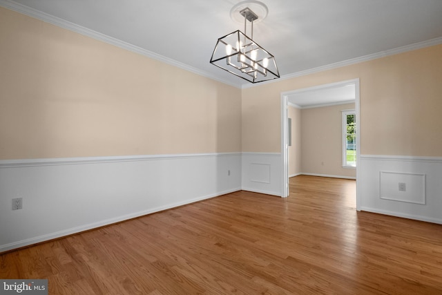 unfurnished dining area featuring an inviting chandelier, light wood-style flooring, crown molding, and wainscoting