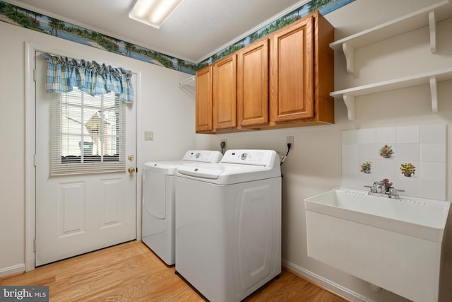 clothes washing area featuring a sink, light wood-style flooring, washing machine and dryer, and cabinet space