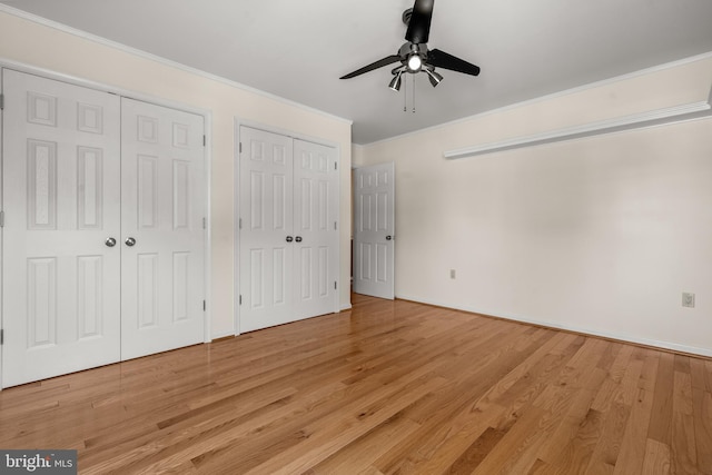 unfurnished bedroom featuring crown molding, a ceiling fan, light wood-style flooring, and two closets