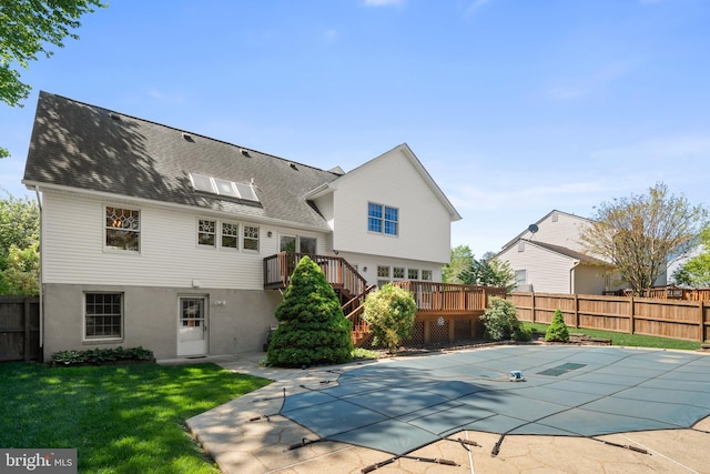 rear view of house with a shingled roof, a wooden deck, a fenced backyard, a fenced in pool, and a lawn