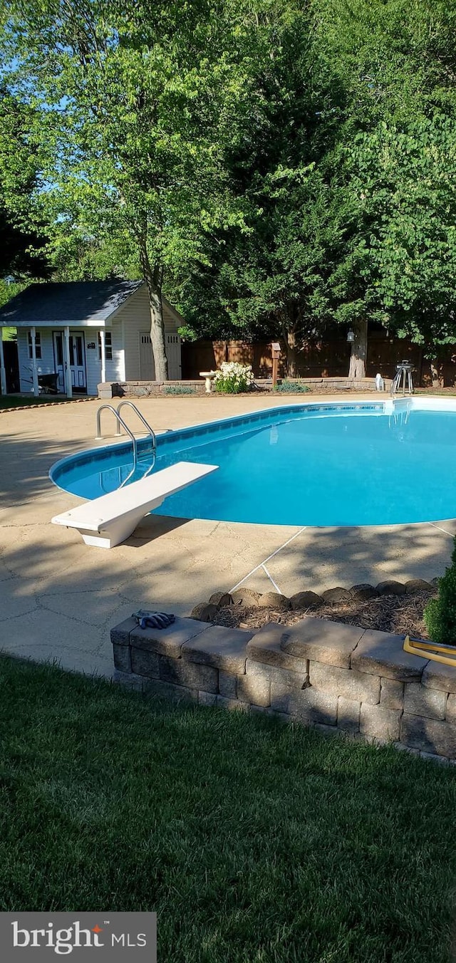 outdoor pool with a diving board, a patio area, and fence