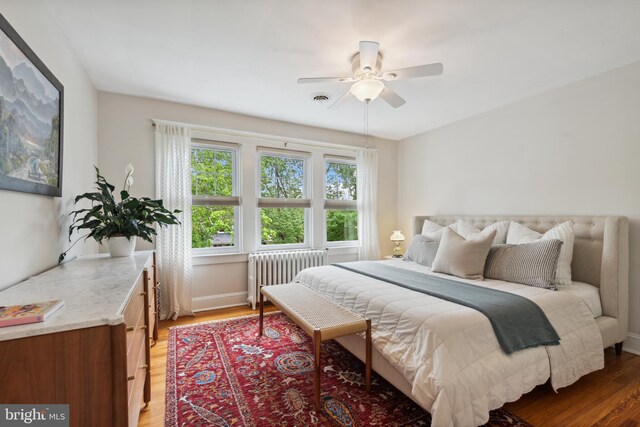 bedroom with radiator, light wood-style floors, a ceiling fan, and baseboards