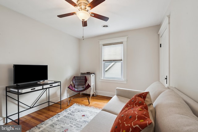 living area with radiator heating unit, wood finished floors, a ceiling fan, and baseboards