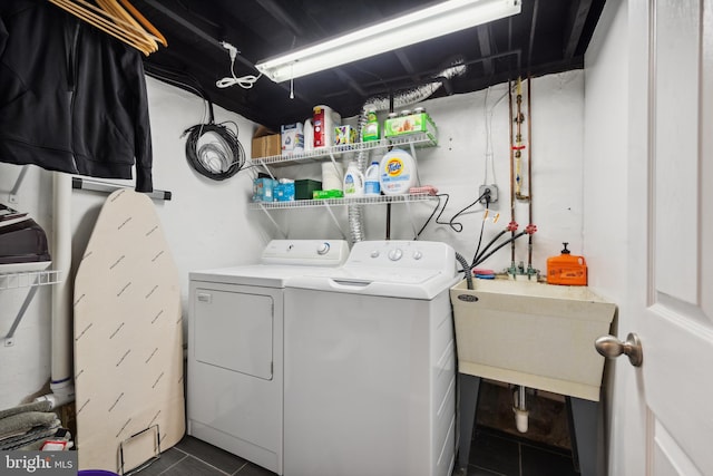 laundry room with washing machine and clothes dryer, dark tile patterned flooring, and a sink
