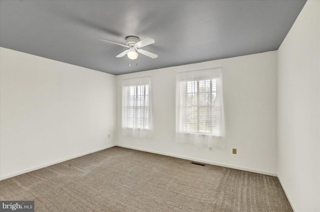 carpeted empty room with visible vents, ceiling fan, and baseboards