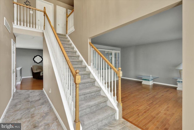 stairway featuring wood finished floors, visible vents, baseboards, and a high ceiling