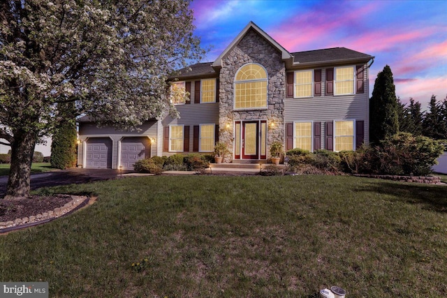 view of front of house featuring driveway, a yard, stone siding, and an attached garage