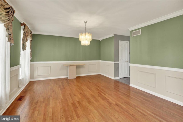 unfurnished dining area with wood finished floors, visible vents, a wainscoted wall, and a chandelier