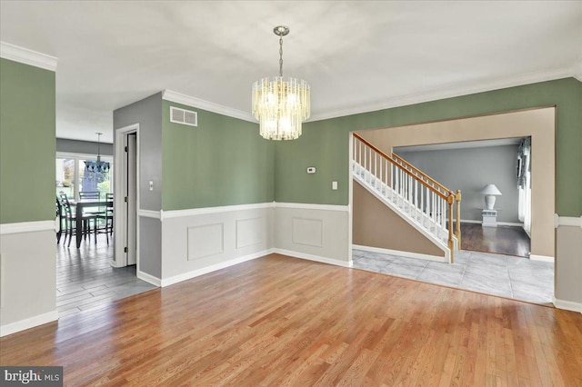 unfurnished dining area featuring crown molding, visible vents, wood finished floors, a notable chandelier, and stairs