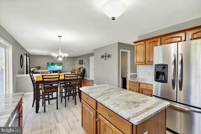 kitchen with a center island, open floor plan, stainless steel fridge with ice dispenser, and light stone counters