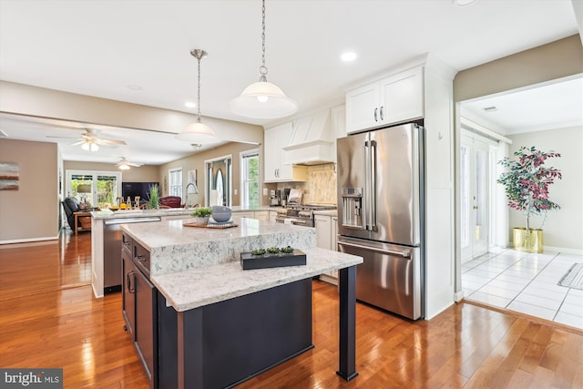 kitchen featuring light wood-style floors, appliances with stainless steel finishes, custom range hood, and a peninsula
