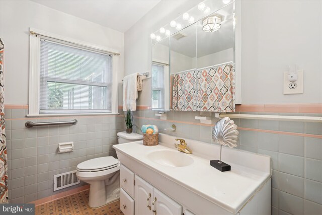bathroom with vanity, toilet, a wainscoted wall, tile walls, and visible vents