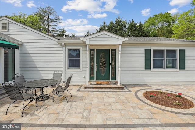 entrance to property with a patio, outdoor dining space, and roof with shingles