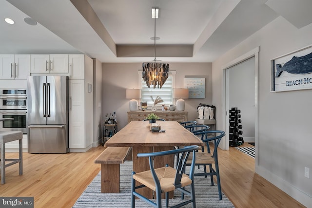 dining area featuring a raised ceiling, baseboards, light wood finished floors, and a chandelier