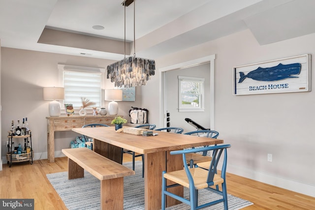 dining area featuring baseboards, light wood-style flooring, a raised ceiling, and a chandelier
