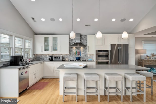 kitchen with appliances with stainless steel finishes, wall chimney exhaust hood, vaulted ceiling, a sink, and tasteful backsplash