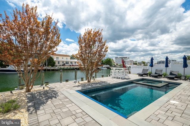 view of swimming pool featuring a patio area, a pool with connected hot tub, a water view, and fence