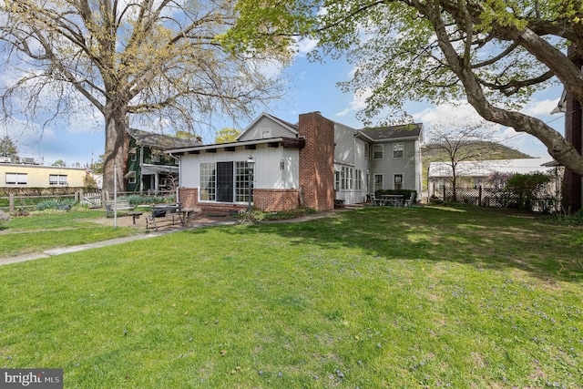 back of property with a chimney, brick siding, fence, and a yard