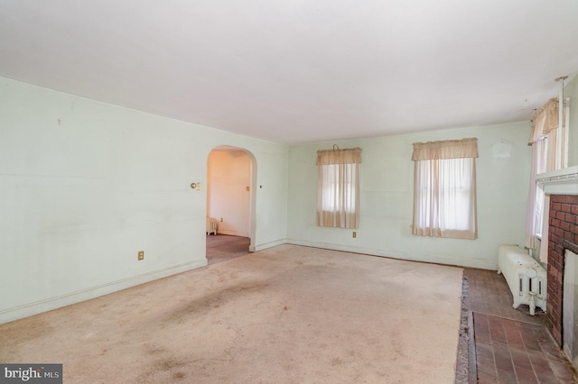 unfurnished living room with a fireplace, baseboards, arched walkways, and radiator