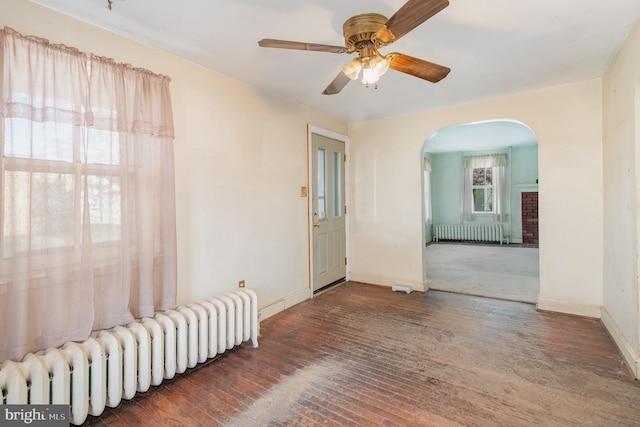 spare room with ceiling fan, hardwood / wood-style floors, arched walkways, and radiator