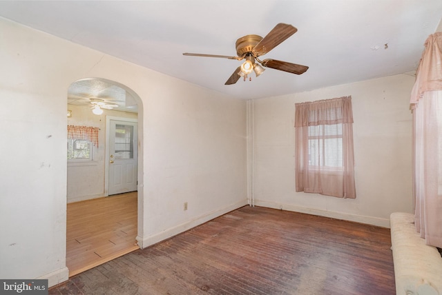 empty room with radiator, arched walkways, ceiling fan, and wood finished floors