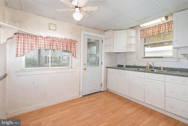 kitchen with a sink, open shelves, light wood-type flooring, white cabinetry, and dark countertops
