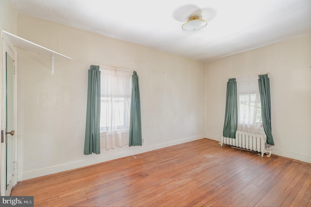 unfurnished room featuring radiator heating unit, light wood-style flooring, and baseboards
