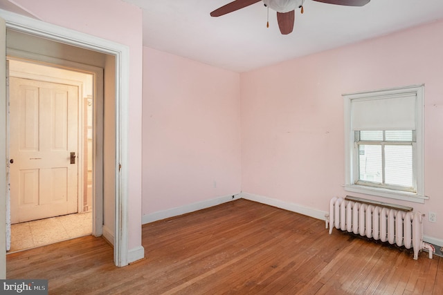 unfurnished bedroom with wood-type flooring, ceiling fan, radiator heating unit, and baseboards