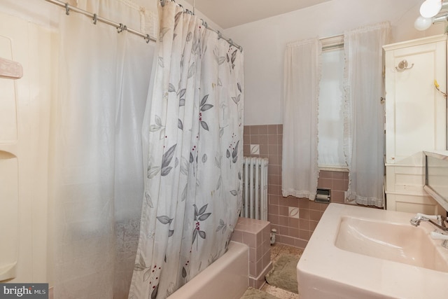 full bath featuring a sink, a wainscoted wall, radiator, shower / bath combo with shower curtain, and tile walls