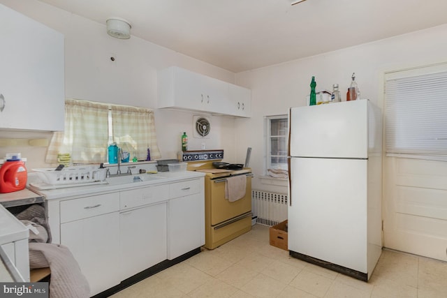 kitchen featuring white appliances, light countertops, radiator heating unit, a sink, and white cabinetry
