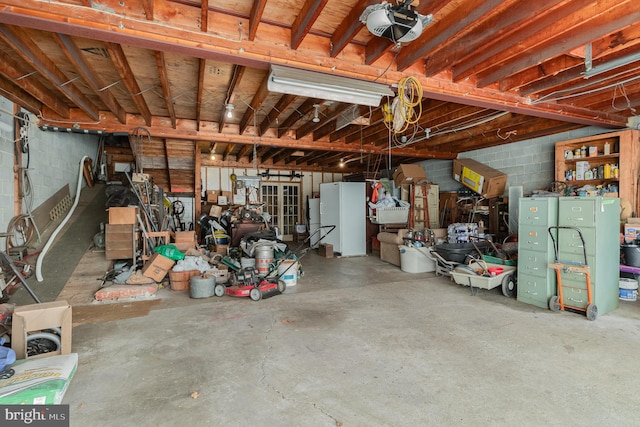garage featuring concrete block wall, freestanding refrigerator, and a garage door opener