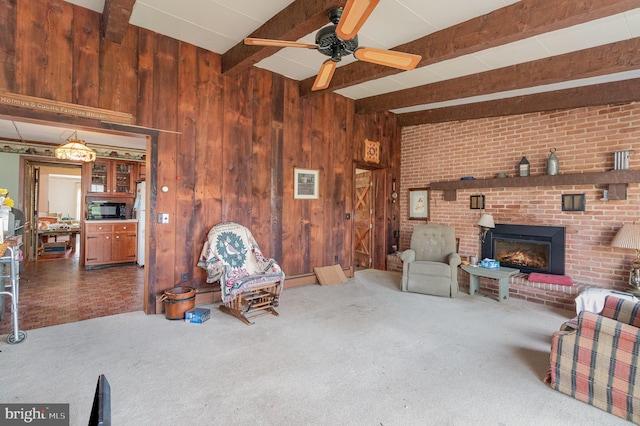 living room with beamed ceiling, wood walls, ceiling fan, a brick fireplace, and carpet